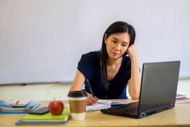 overworked asian businesswoman working hard on laptop in bright home office stock photo