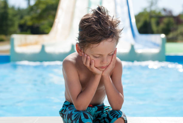 niño triste solitario sentado cerca de la piscina de agua en el parque acuático del complejo de verano - swimming pool water people sitting fotografías e imágenes de stock