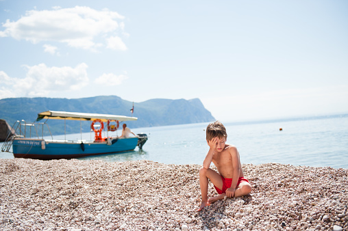 sun stroke health concept of cute small boy sitting on heat beach on summer sunny day on beautiful island