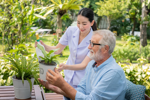istock Caregiver help assist senior old man eldery puring water and taking care small tree on table 1166772018