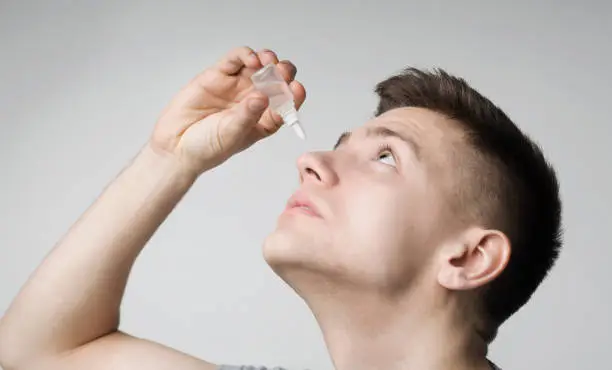 Photo of Young guy using disease contact eye drop, applying medicament