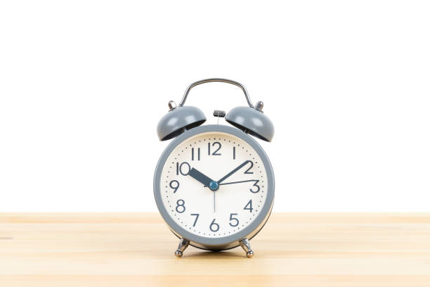 istock Grey alarm clock on wooden desk on white background 1166773640