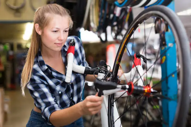 Portrait of happy female who is repairing wheels of bicycle in workshop indoors