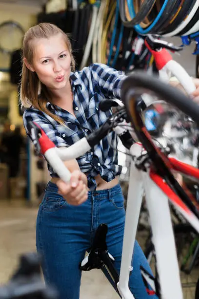 Smiling girl is standing with bicycle in shop