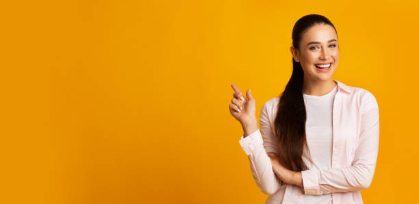 istock Pretty Woman Pointing Finger At Empty Space Over Yellow Background 1166776276