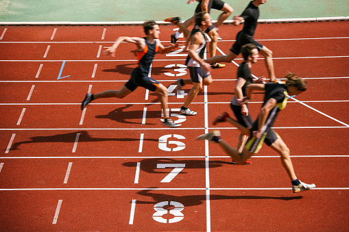 A side shot of a diverse group of females training on a running track. It is a bright day with blue skies. There are no spectators in the frame.