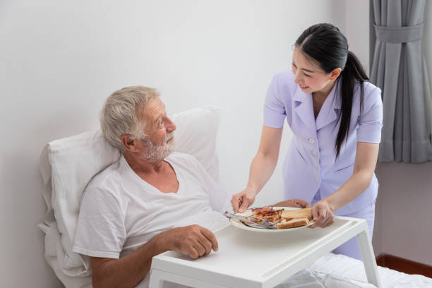 老人ホームの寝室でベッドの上で高齢者の朝食を提供する幸せな看護師 - senior adult nursing home eating home interior ストックフォトと画像