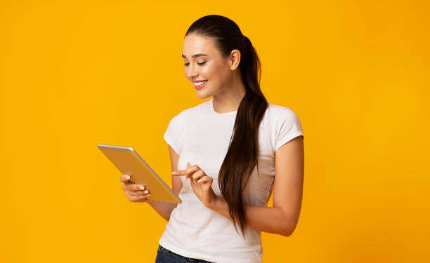 istock Lovely Girl Using Digital Tablet Over Yellow Studio Background 1166779028