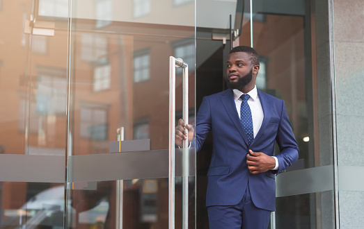 Handsome confident african businessman in formal suit walking out of modern office center, copy space