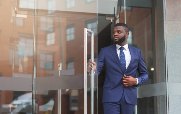 Confident african businessman walking out of modern office center Handsome confident african businessman in formal suit walking out of modern office center, copy space office leave stock pictures, royalty-free photos & images