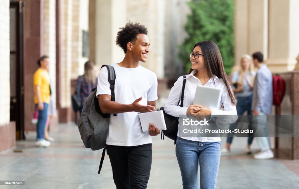 Amici del college che camminano nel campus e parlano - Foto stock royalty-free di Studente universitario