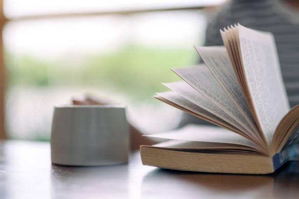 istock a woman holding and reading a book while drinking coffee 1166782743