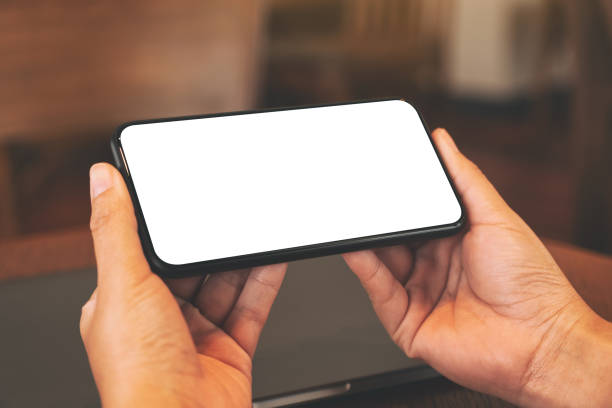 istock hands holding black mobile phone with blank desktop screen with laptop computer 1166783295