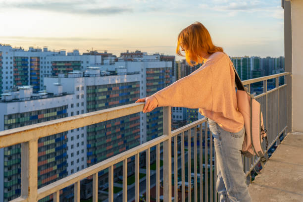 istock Tween redhead girl in pullover, jeans and sunglasses standing on balcony against high-rise multi-storey residential building at sunset. Beautiful look, fashionable city street outfit, teenage fashion 1166784019