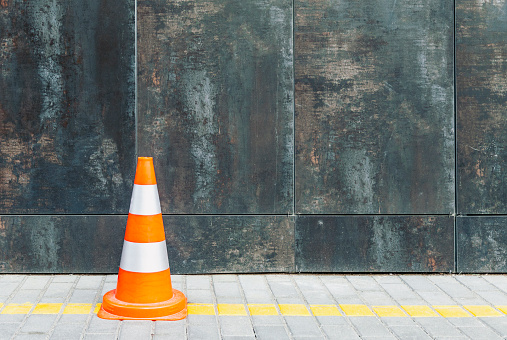 Plastic traffic cone against grunge wall with copy space, road cone and bollard standing on pavement