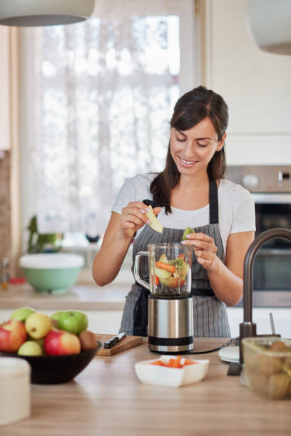 istock Woman putting vegetables and fruits in blender while standing in kitchen. 1166789546