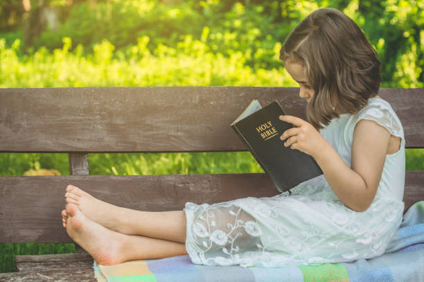 Reading the Holy Bible in outdoors. Christian girl holds bible in her hands sitting on a bench. Concept for faith, spirituality and religion Reading the Holy Bible in outdoors. Christian girl holds bible in her hands sitting on a bench. Concept for faith, spirituality and religion. Peace, hope Bible stock pictures, royalty-free photos & images