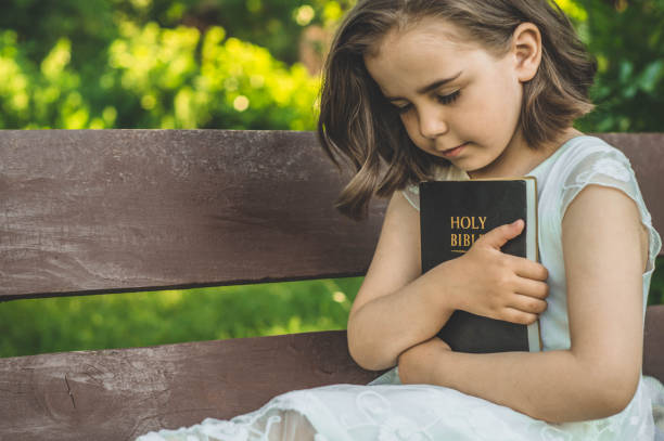 leyendo la santa biblia al aire libre. la chica cristiana sostiene la biblia en sus manos sentada en un banco. concepto de fe, espiritualidad y religión - praying girl fotografías e imágenes de stock