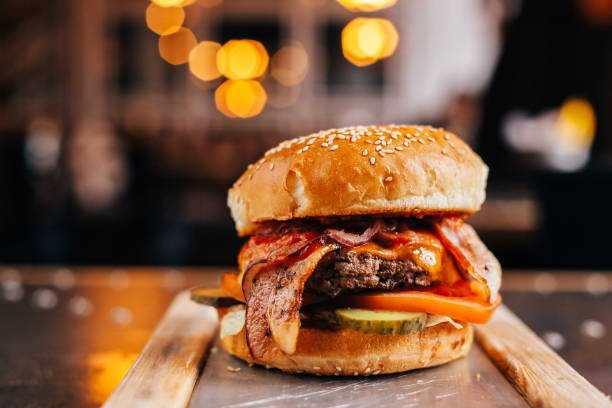 Burger with beef and bacon Burger with a cutlet of murbled beef with cheddar cheese, bacon, spicy chili sauce, cucumber and tomato, in a white bun with sesame seeds served burger close up stock pictures, royalty-free photos & images