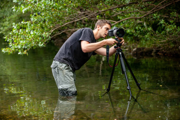 istock Photographer setting his camera on the tripod while standing in a shallow water stream 1166798349