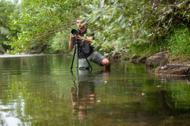 young photographer capturing an image from an uncomfortable position in the middle of the river - reportagem imagens e fotografias de stock