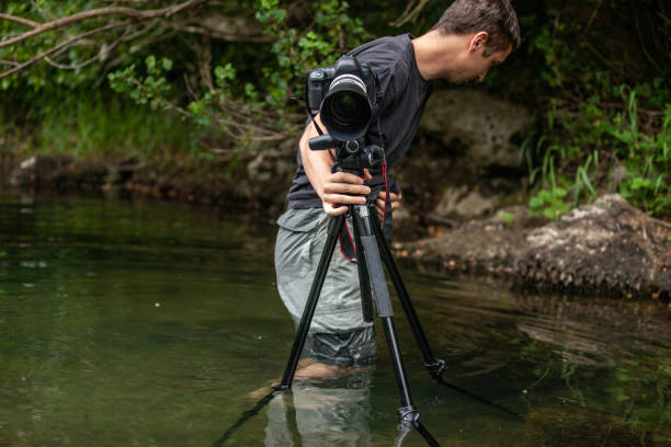 istock Photographer setting his camera on the tripod while standing in a shallow water stream 1166798645
