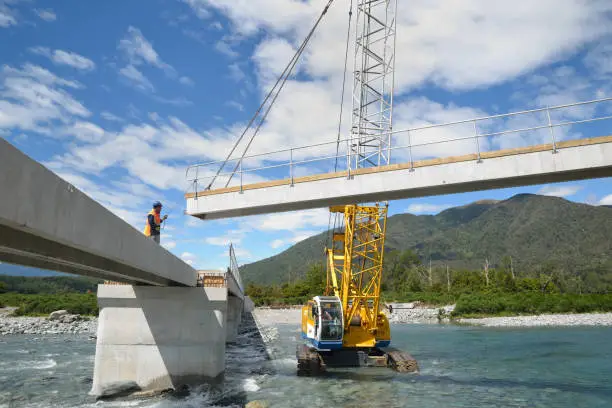 Builders construct a concrete bridge over a small river in Westland, New Zealand