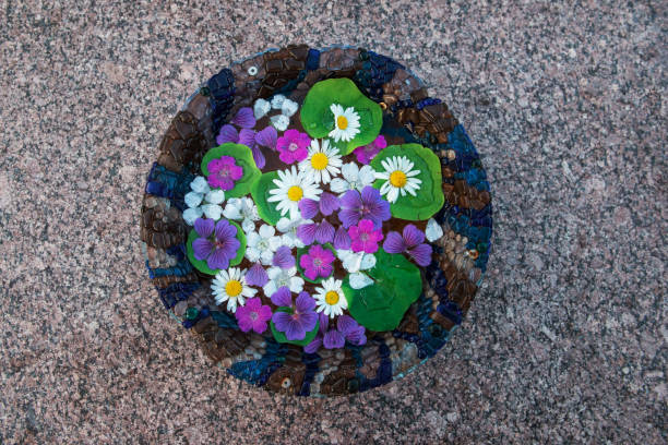 Bowl with water and flowers on gray stone background, top vew
