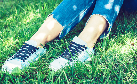 Young woman legs in pair of sport shoes sneakers  of blue suede on the grass lawn in park