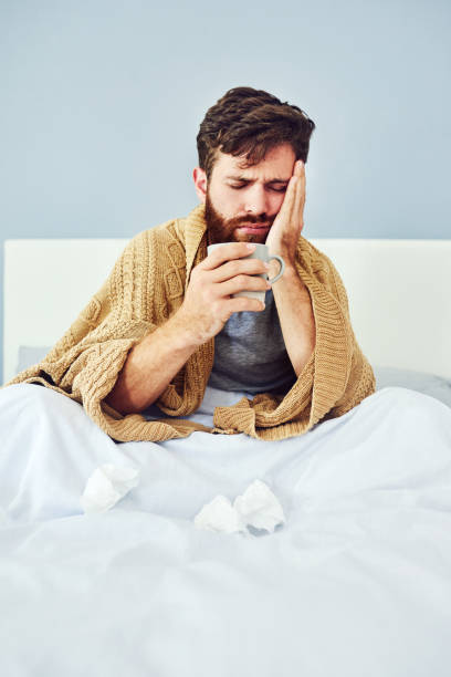 A hot beverage may help ease your symptoms Shot of a young man sitting in bed while suffering with flu cold virus stock pictures, royalty-free photos & images