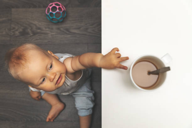 concepto de quemadura y lesión por escaldamiento del niño - niño pequeño que busca la taza de bebida caliente en la mesa - bebida caliente fotografías e imágenes de stock