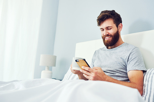 Cropped shot of a young man using his cellphone while relaxing in his bedroom