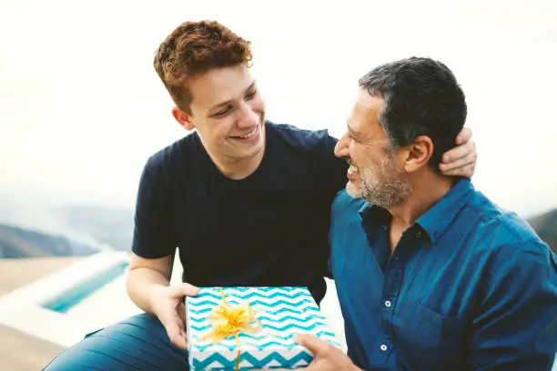 Teenager giving a gift for his father outdoors in the nature.