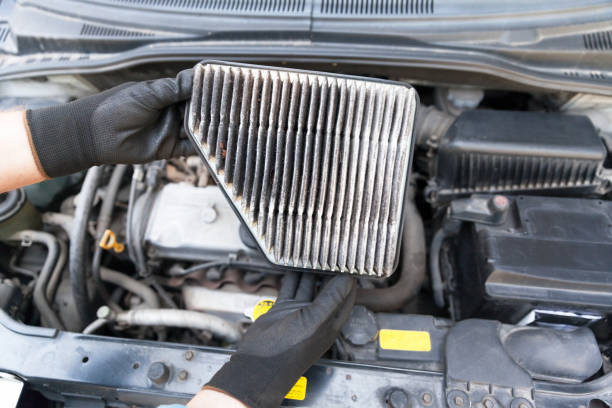 istock Auto mechanic wearing protective work gloves holding dirty air filter above a car engine 1166807006