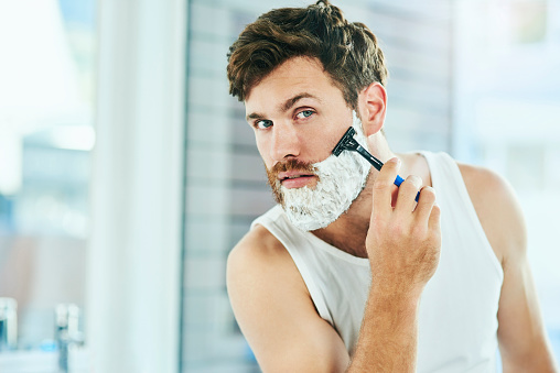 Cropped shot of a handsome young man shaving his beard in the bathroom at home