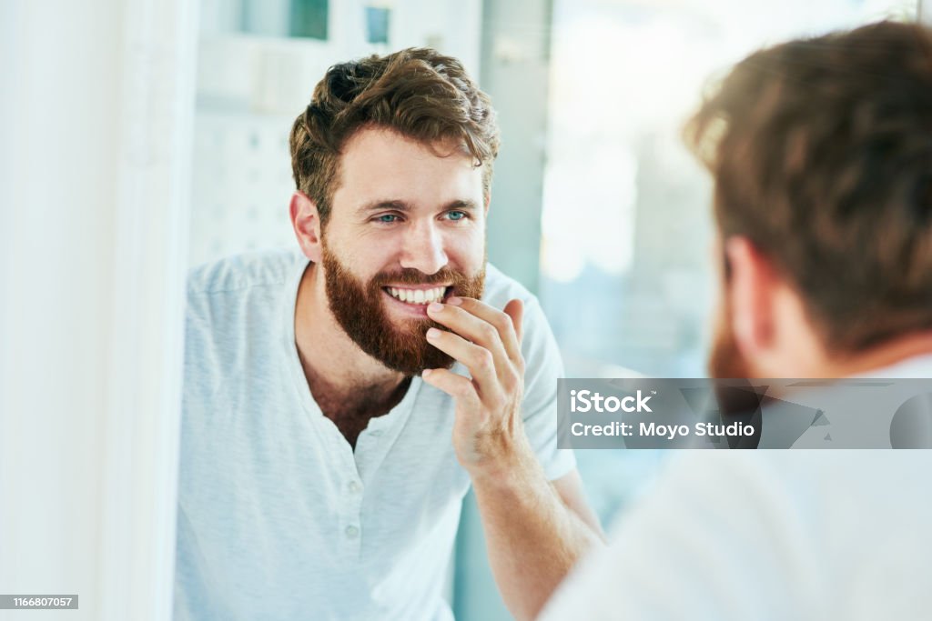 I've never seen a smile more perfect Cropped shot of a handsome young man looking at his teeth in the bathroom mirror Teeth Stock Photo