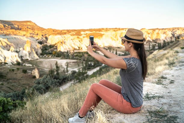 istock Young Woman Taking Photos With Smartphone Sitting In Front Of Valley 1166808564