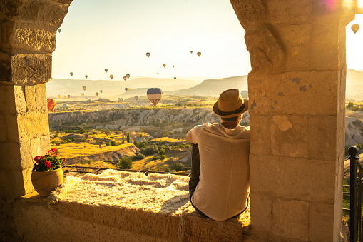 Rear View Of A Young Man Sitting And Looking At View During Ballooning Festival