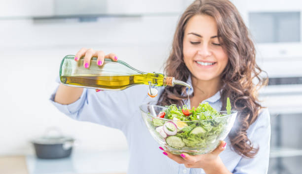 молодая женщина наливает оливковое масло в салат. здоровый образ жизни есть концепция. - cooking oil oil pouring olive oil стоковые фото и изображения