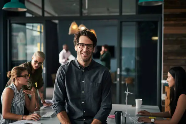 Portrait of a handsome businessman standing inside an office with his colleagues working in the background