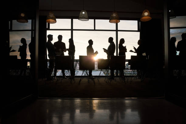 Everything we've been working on will come to light soon Full length silhouetted shot of a group of businesspeople working and conversing together inside a modern office business people silhouette stock pictures, royalty-free photos & images