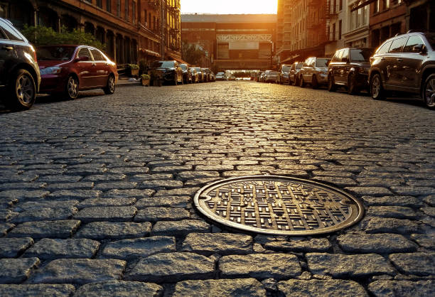 Sunlight shining on a cobblestone street and manhole cover in New York City Sunlight shining on a cobblestone street and manhole cover in Manhattan New York City NYC manhole stock pictures, royalty-free photos & images