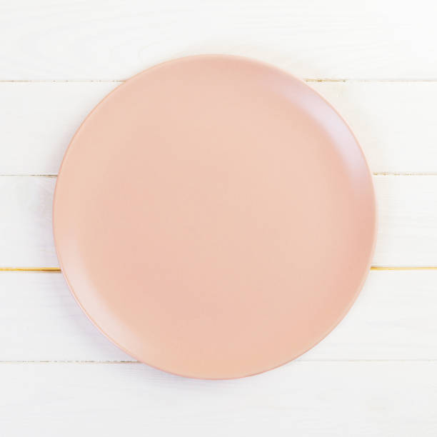 istock Empty pink or coral round plate on wooden table background. Top view, template for your design 1166814809