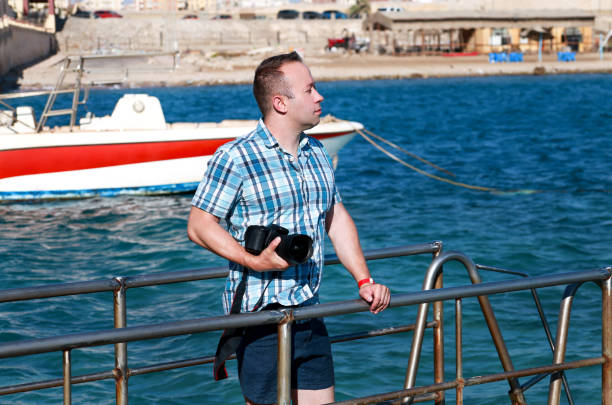 Professional photographer, tourist and traveler on sea pier is taking picture of environment, sea coast. Man on vacation in hotel resort on beach platform, he making landscape photography with camera. fotógrafo profesional, turista y viajero en el muelle del mar está tomando fotos de medio ambiente, costa del mar. hombre de vacaciones en el complejo del hotel en la plataforma de la playa, que hace la fotografía del paisaje con la cámara.