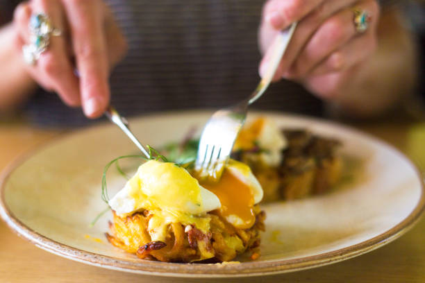 Woman Eating Poached Eggs Benedict (with Fried Potatoes) Close-Up. Shot in Holland.