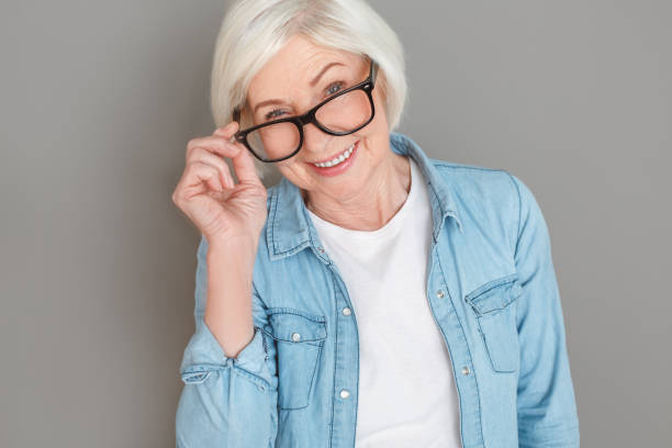 istock Senior woman in jeans jacket studio isolated on grey wall touching glasses looking camera 1166818555