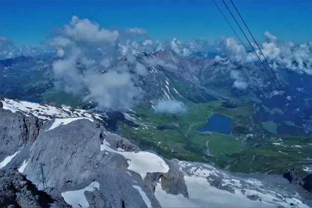 A spectacular series of 3 panoramic images of the high peaks of central Switzerland on an especially clear day in summer 2019. They are taken from the high altitude Cable-way "Titlis" that links Engelberg to Trüebsee and ultimately on to the permanent snow-ski slopes of Mount Titlis. The sheer expanse and grandeur of this unique landscape is perfectly captured with visibility on that day of over 80 miles at an altitude of around 10,000 ft, you can see virtually the whole of Central Switzerland in one view, simply by being in the right place at the right time. These shots are all taken looking down from the cable car and one can see the edge of the snowline very clearly - the softer, less harsh green mountains and alpine pastures are all far below. This second image looks due north towards Luzern and Zurich and the lake at the resort of Trüebsee can be clearly seen as the source of this stretch of the cable way.