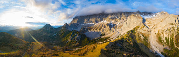 beautfiul aerial panorama view in mountain landscape sunrays over alpine pasture valley timber line rocky mountains summit covered with clouds