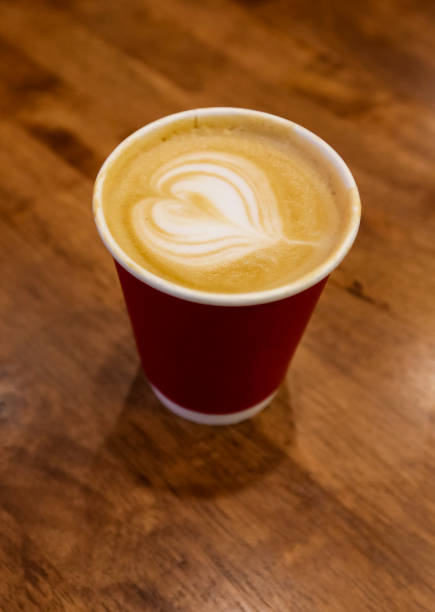 Paper cup of cafe latte on wooden table background. Art style hot coffee. A latte is a coffee drink made with espresso and steamed milk.
