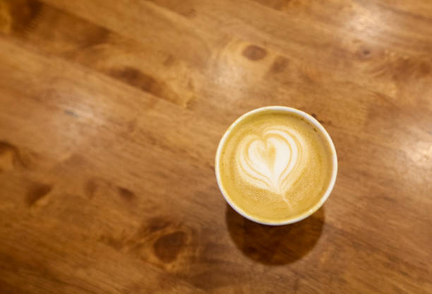 Paper cup of cafe latte on wooden table background. Art style hot coffee. A latte is a coffee drink made with espresso and steamed milk.